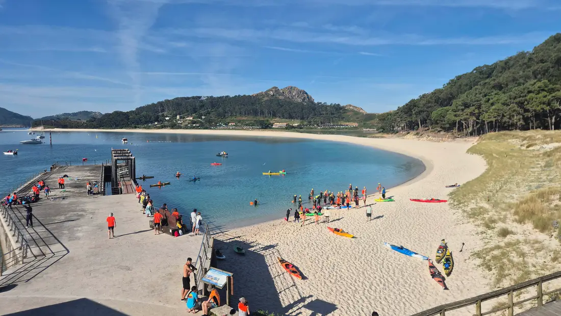 La playa de Rodas, en las Islas Cíes, con los nadadores reuniéndose en la orilla y los kayaks varados en la arena