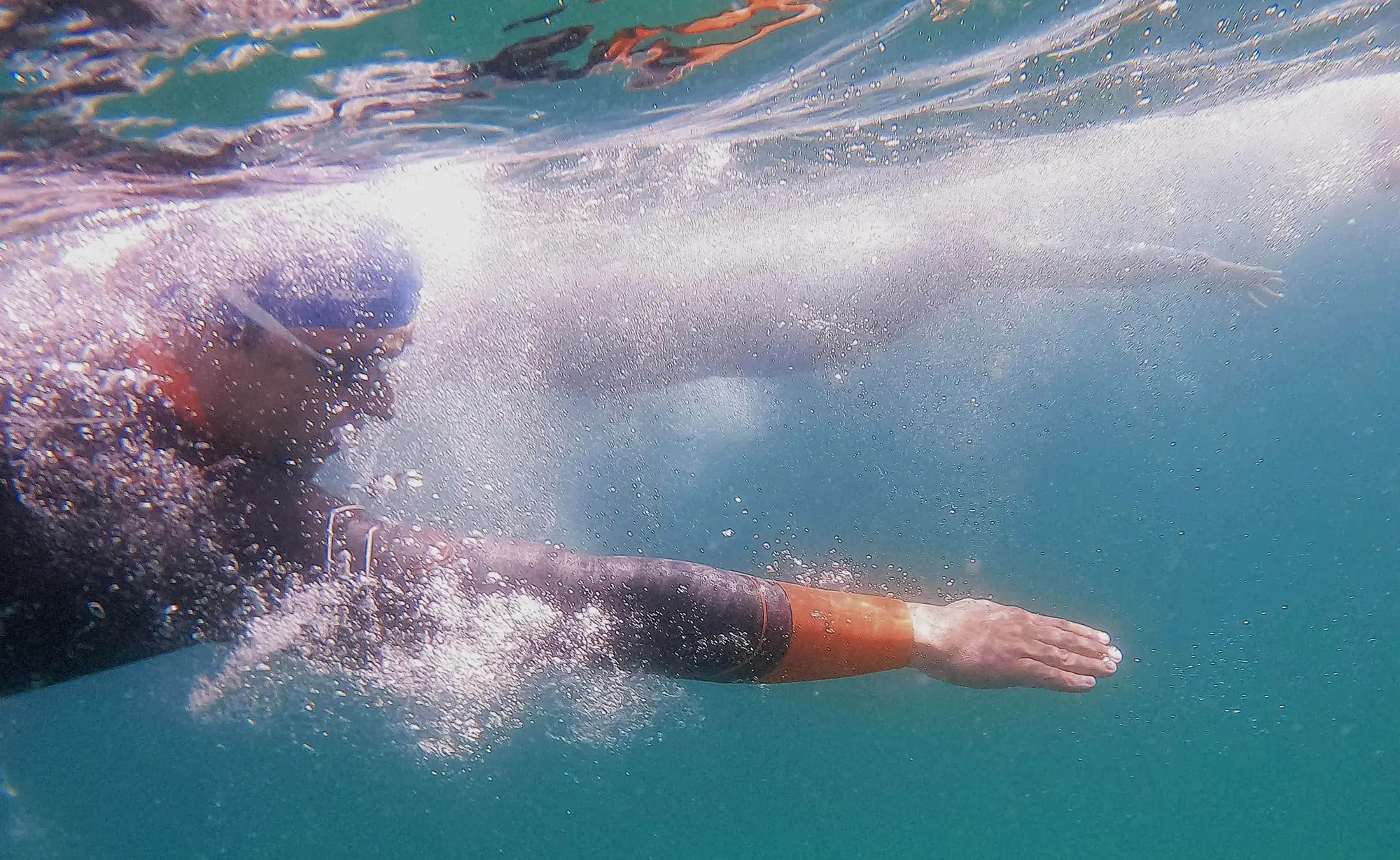 Un nadador visto desde debajo del agua, en pleno brazo de crol, entre burbujas y agua turquesa