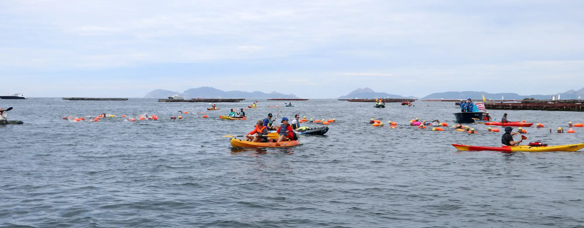 La columna de nadadores, kayaks y lanchas avanzando por la ría de Vigo, con las bateas y las Islas Cíes al fondo
